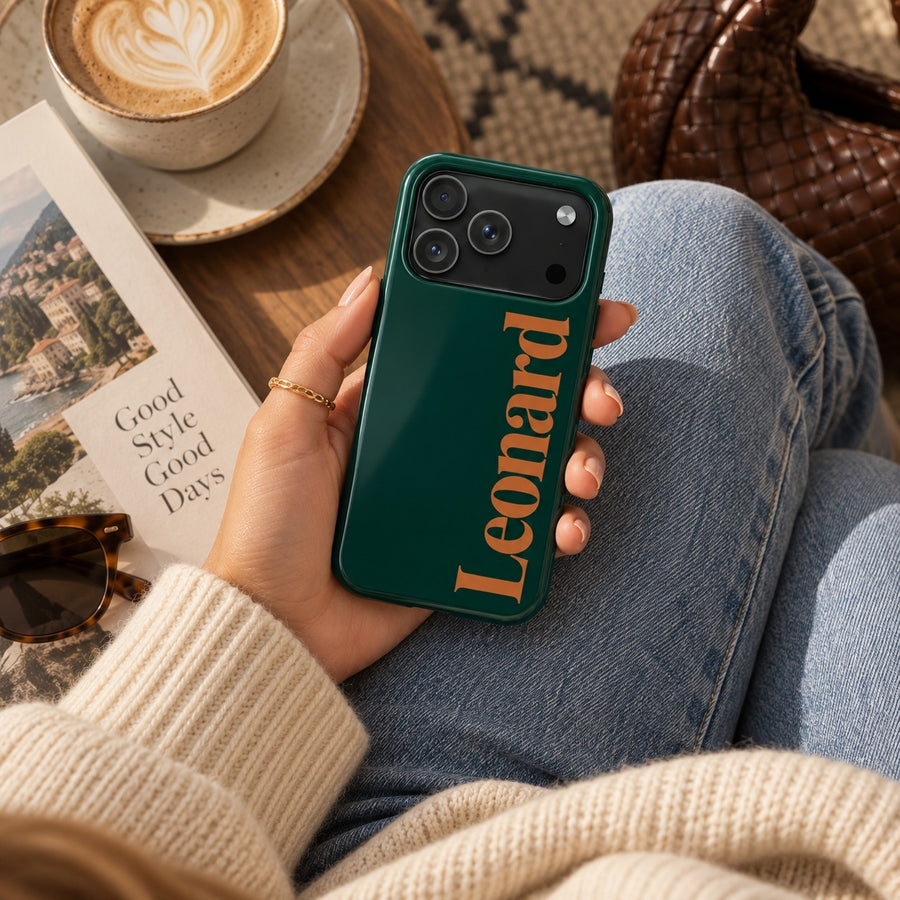 Forest green name case printed with the name Leonard in orange serif lettering, held in one hand beside a coffee cup